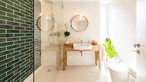 Un baño moderno con cabina de ducha de vidrio, tocador de madera, espejo redondo y inodoro.