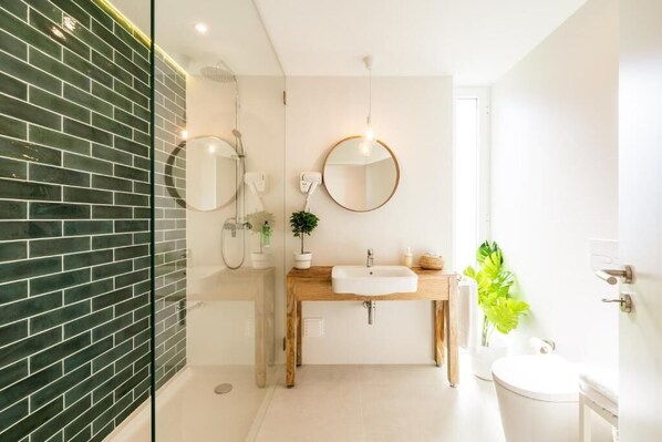 A modern bathroom with a glass shower enclosure, a wooden vanity, a round mirror, and a toilet. - Casa Vica - Sagres Apartments (Vila do Bispo)