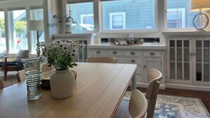 Uma cozinha moderna com armários brancos, uma mesa de jantar de madeira e um vaso com flores.