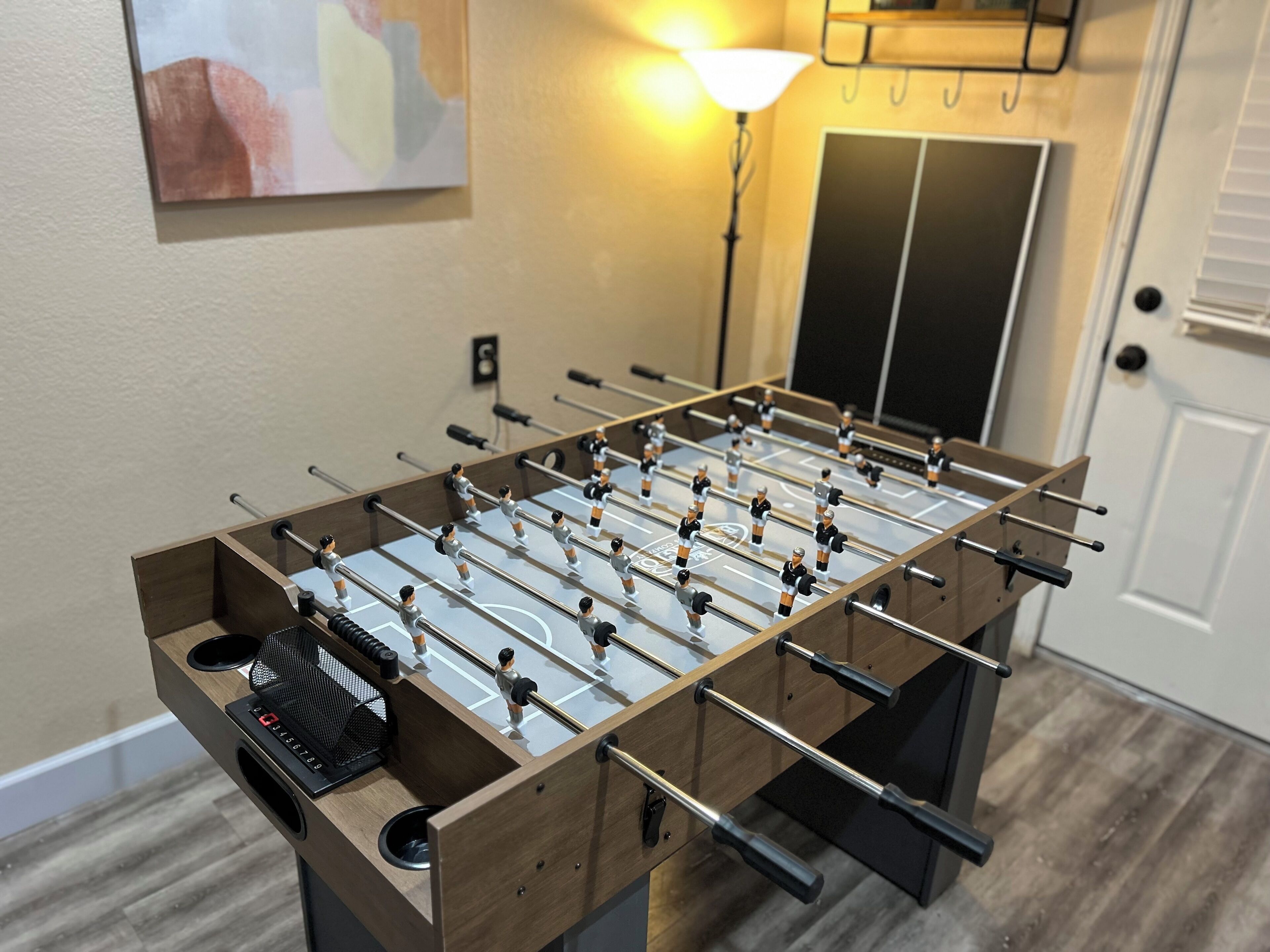 A foosball table in a room with a door and a wall-mounted artwork.