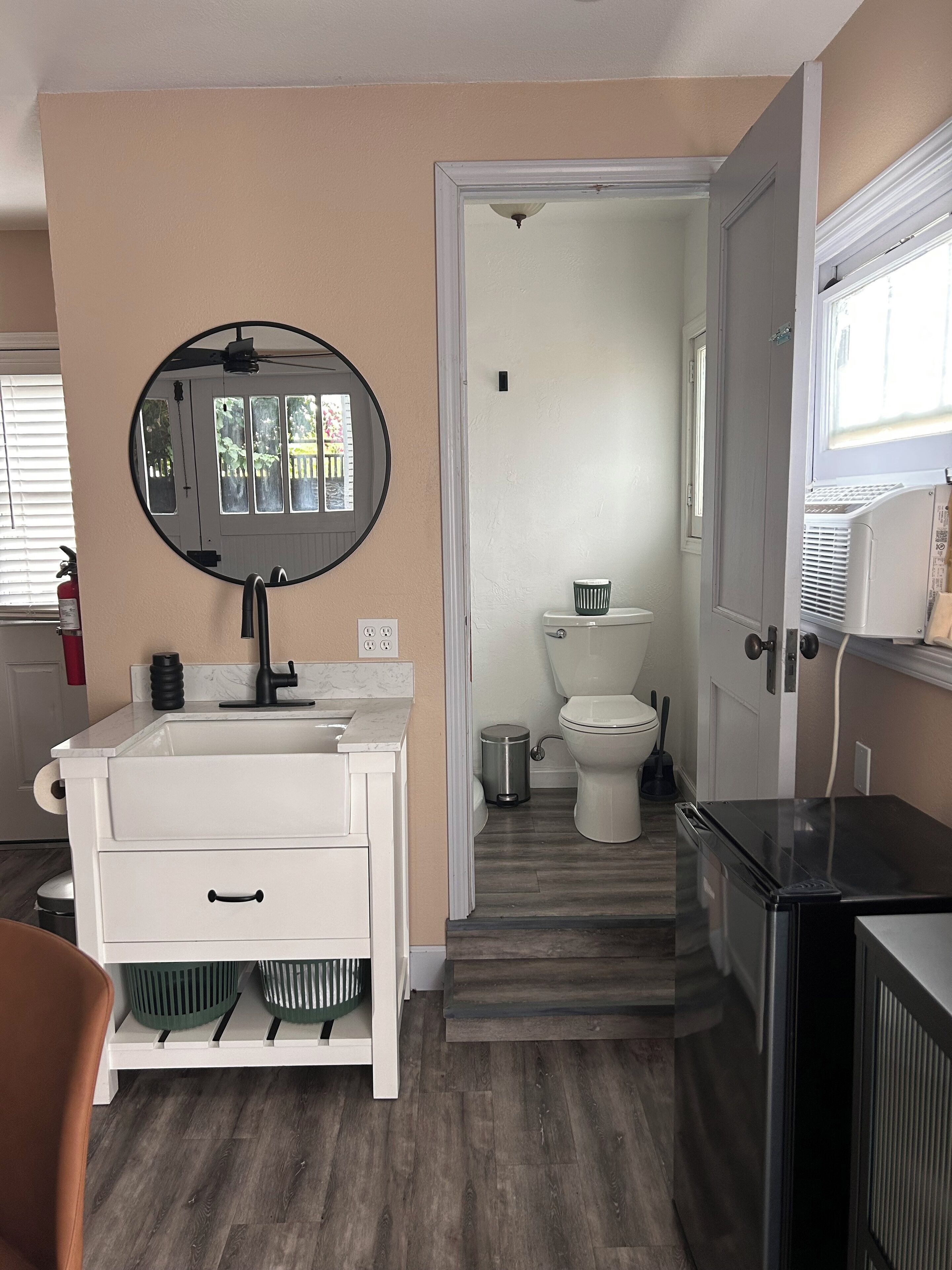 A compact bathroom with a white vanity, a round mirror, a toilet, and a heater.