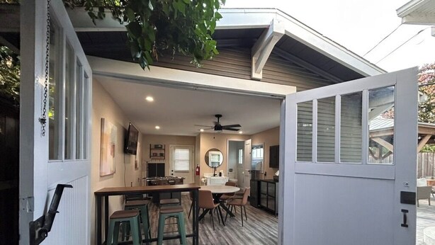 Garagem aberta que dá para uma área de jantar com mesa e cadeiras, um ventilador de teto e uma cozinha visível ao fundo.
