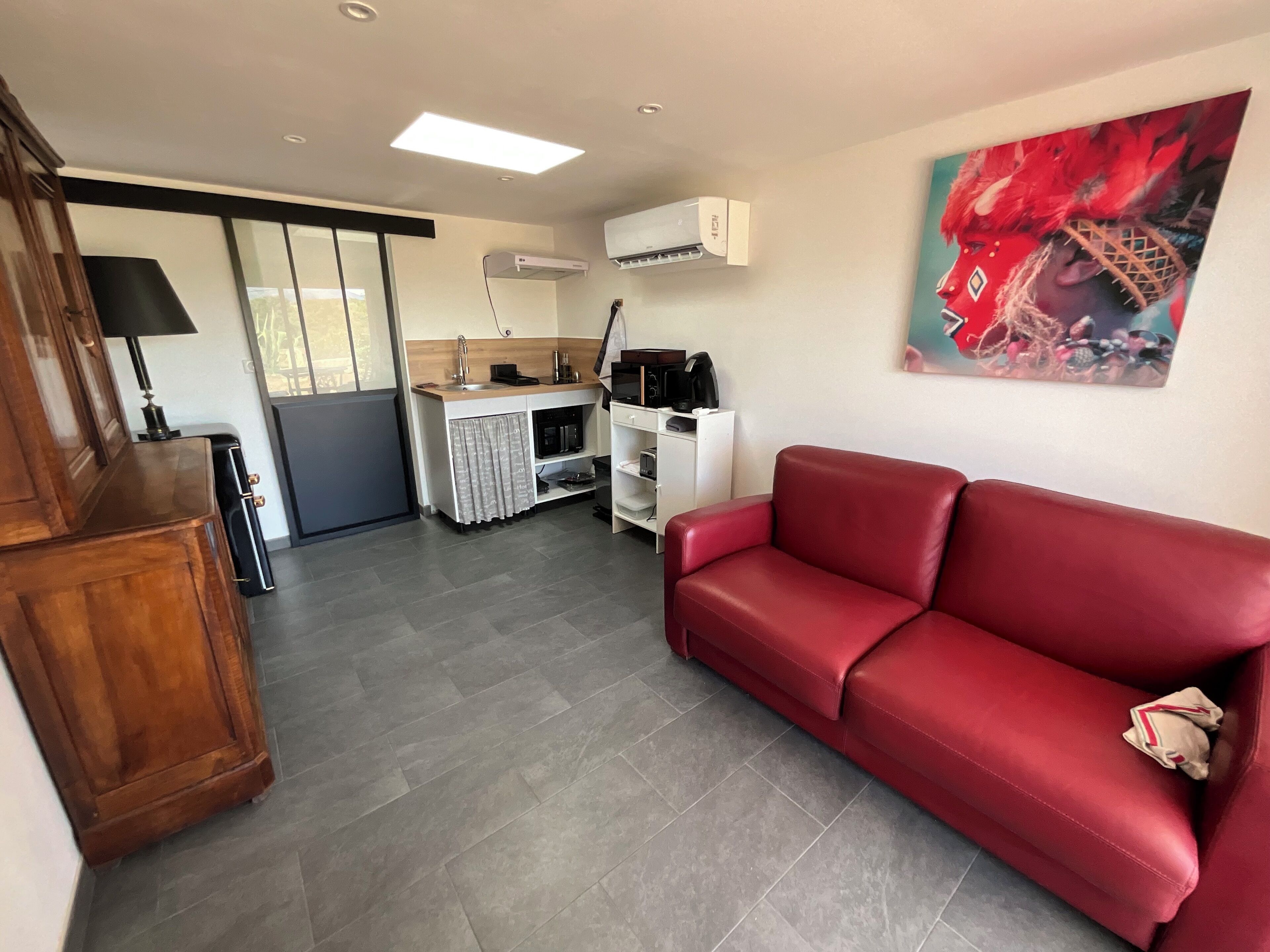 A compact living space with a kitchenette, a red leather sofa, and a painting on the wall.