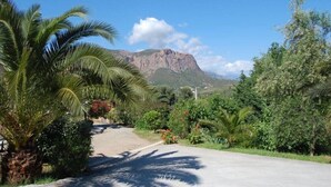 A road with a mountain in the background, surrounded by lush greenery and palm trees. - Studio room with jacuzzi and heated swimming pool 4X8 (Alata)