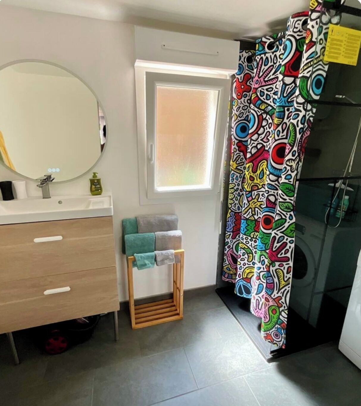 A bathroom with a white sink, a mirror, a wooden vanity, a towel rack, and a colorful shower curtain.