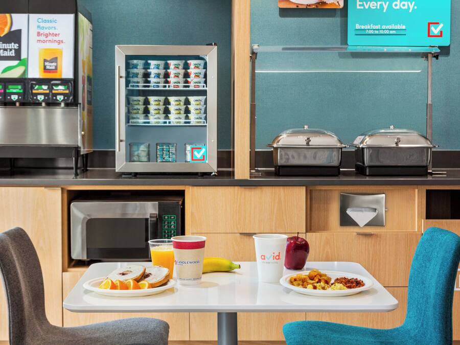 A breakfast area with a vending machine, a refrigerator, and a microwave. There are two chairs and a table with breakfast items.