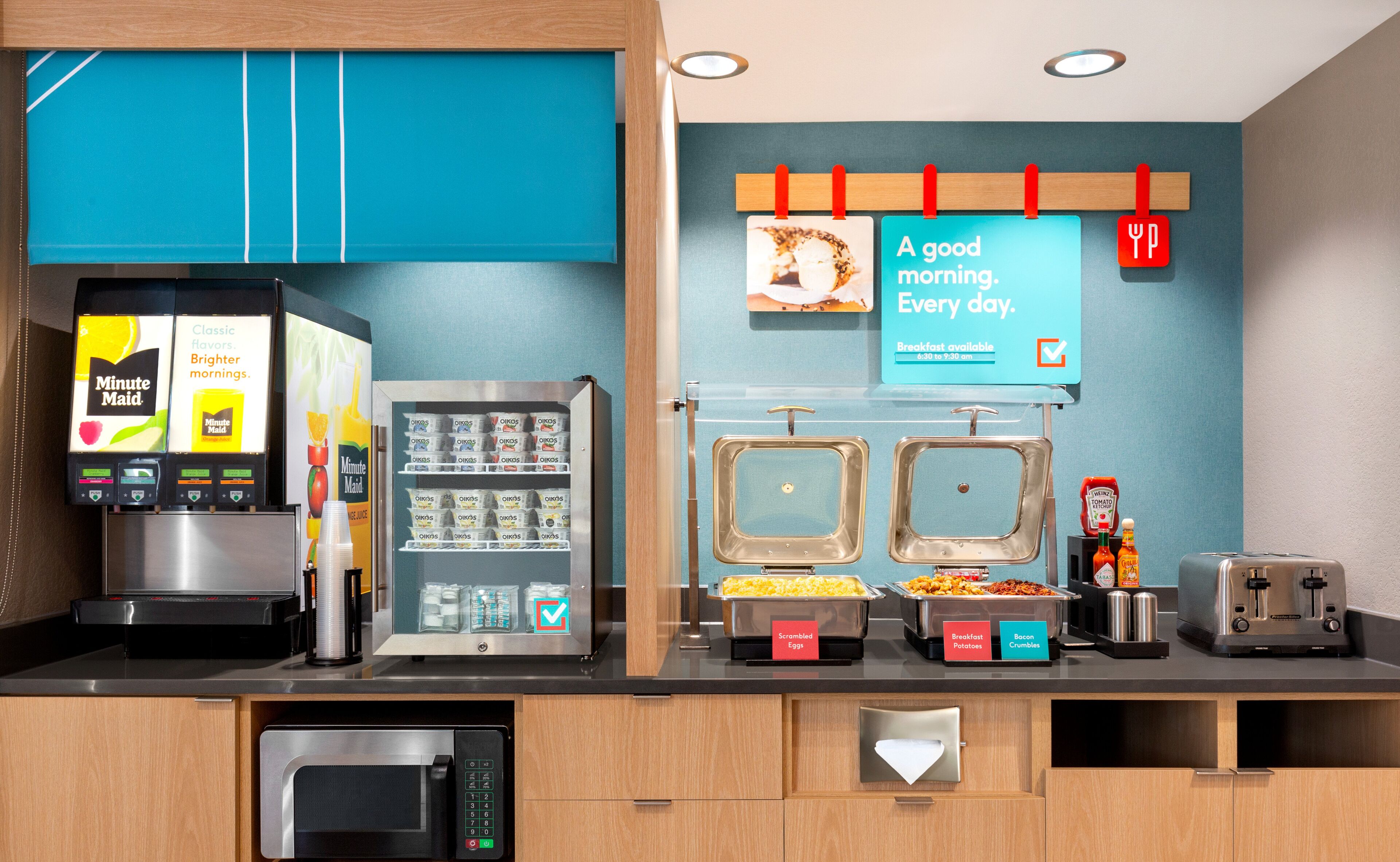 A breakfast station with a coffee machine, a refrigerator with beverages, and labeled food containers.