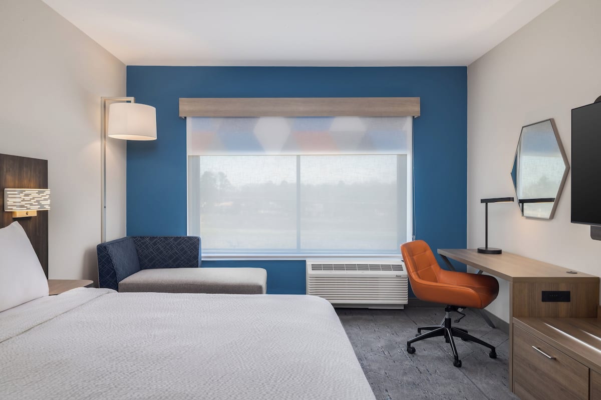 Ett hotellrum med en säng, två stolar, ett skrivbord, en tv och ett stort fönster med utsikt.