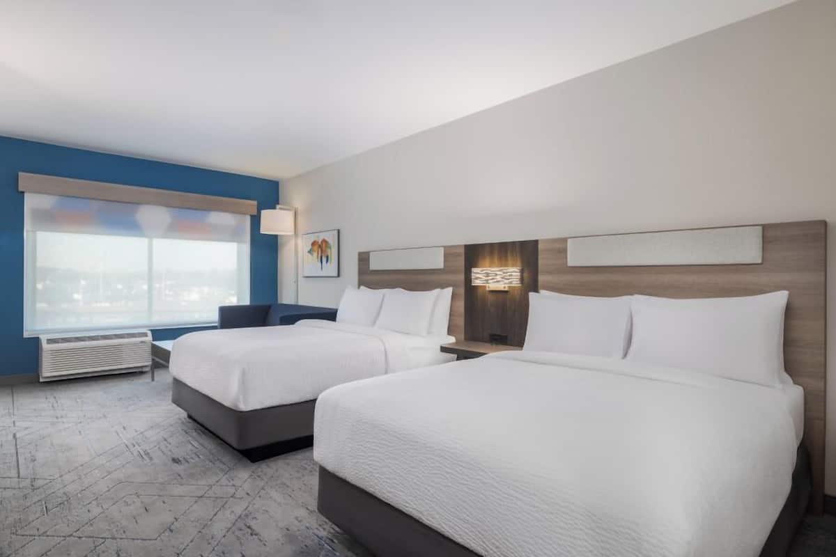 Ett hotellrum med två sängar, ett stort fönster, ett konstverk som hänger på väggen och en modern lampa.