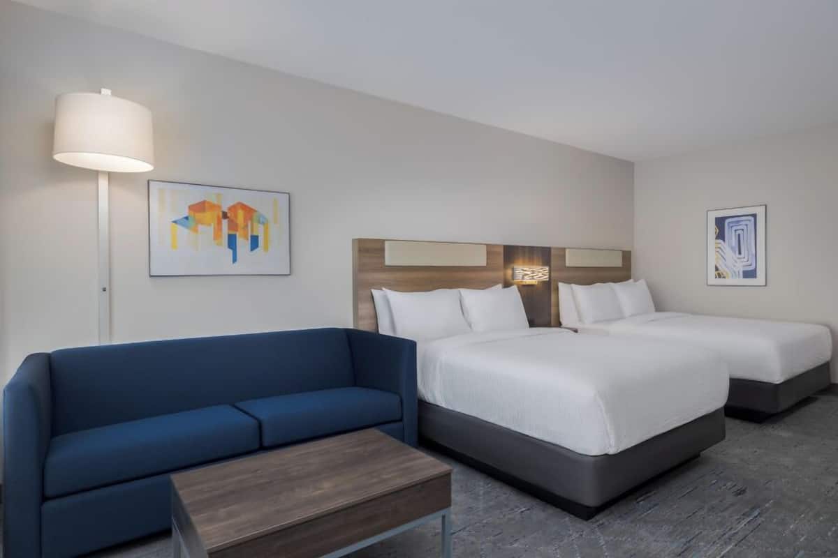 Ett hotellrum med en blå soffa, två enkelsängar, ett träbord vid sängen och en lampa.