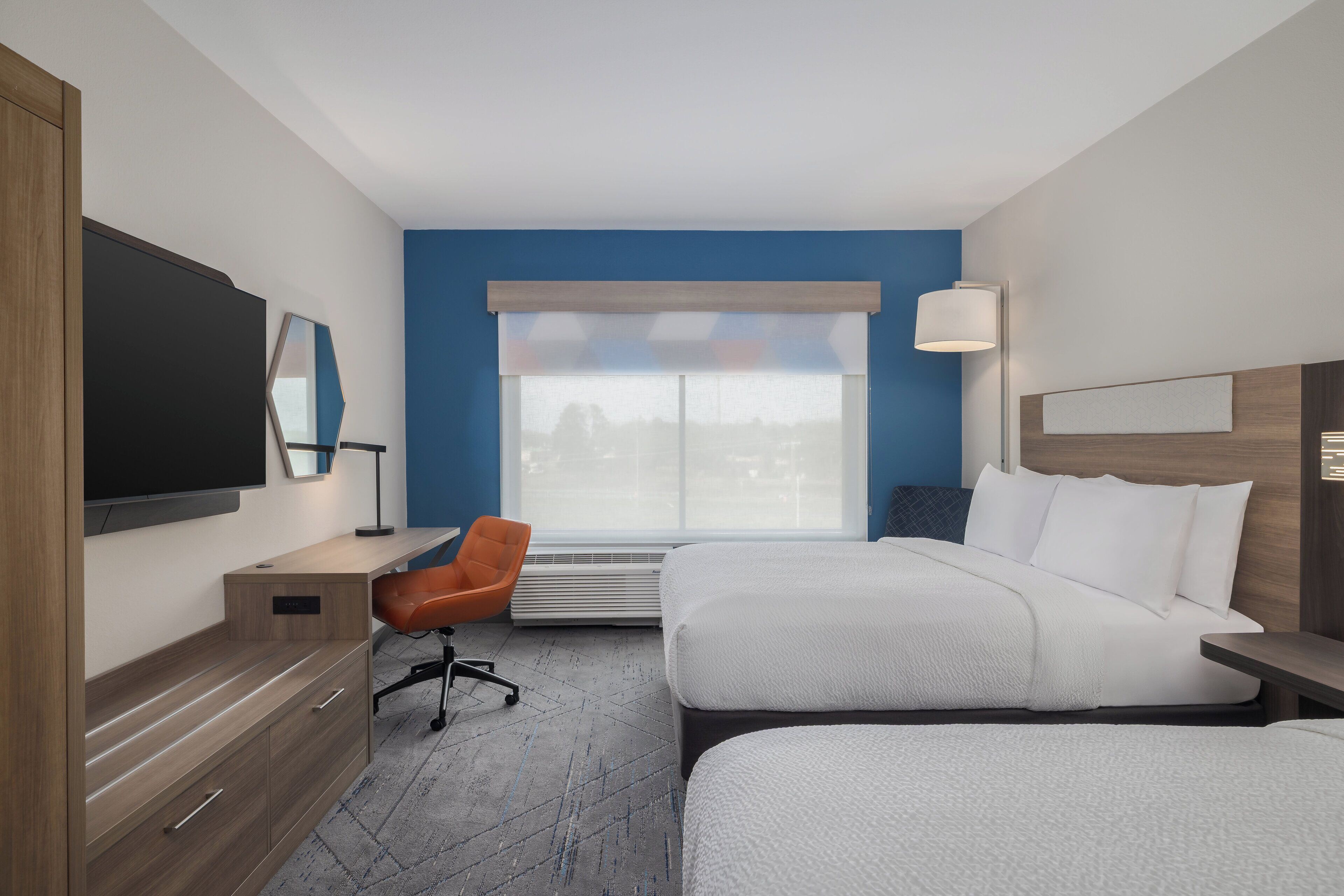 Habitación de hotel con dos camas, un escritorio, una silla, un televisor y una ventana con persianas.