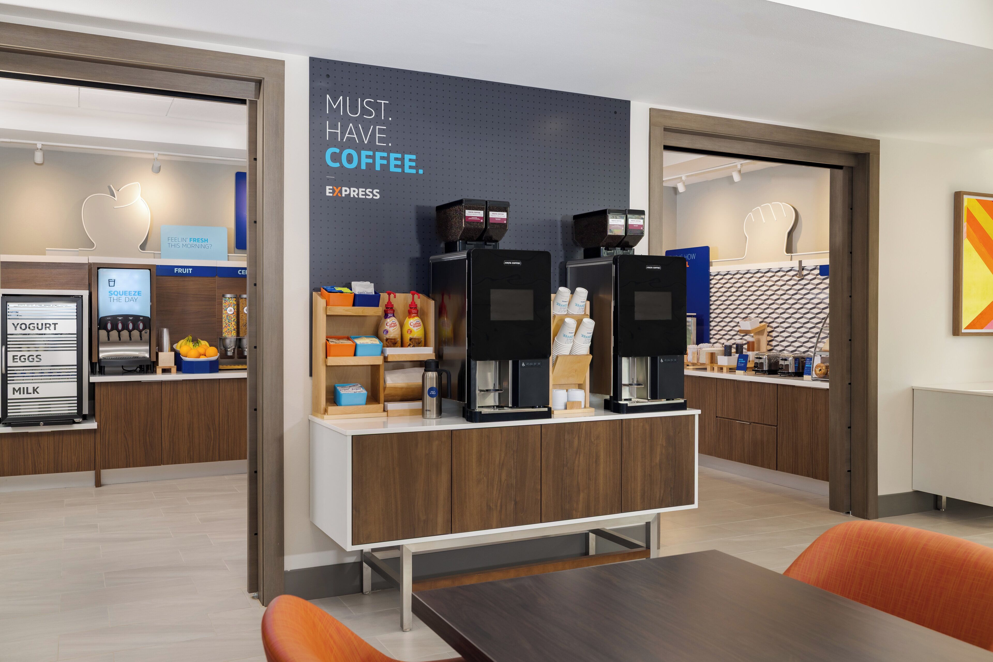 A modern coffee shop with espresso machines, a yogurt fridge, and a fruit display.