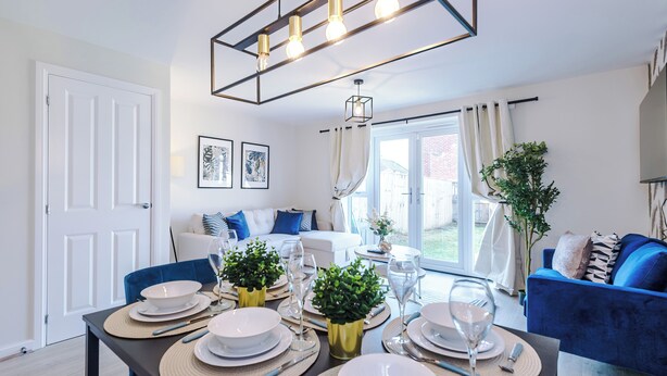Un coin repas avec une table dressée pour quatre personnes, un canapé bleu et une grande fenêtre avec des rideaux.