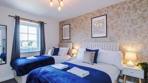 Une chambre d’hôtel avec deux lits, une grande fenêtre avec des rideaux, un luminaire fixé au mur et des œuvres d’art encadrées.