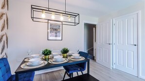 Un coin repas avec une table rectangulaire dressée pour quatre personnes, agrémenté d’un luminaire suspendu au design moderne.