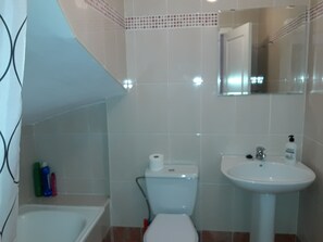 Ein Badezimmer mit Toilette, Waschbecken und Badewanne. An der Wand befinden sich Toilettenartikel.