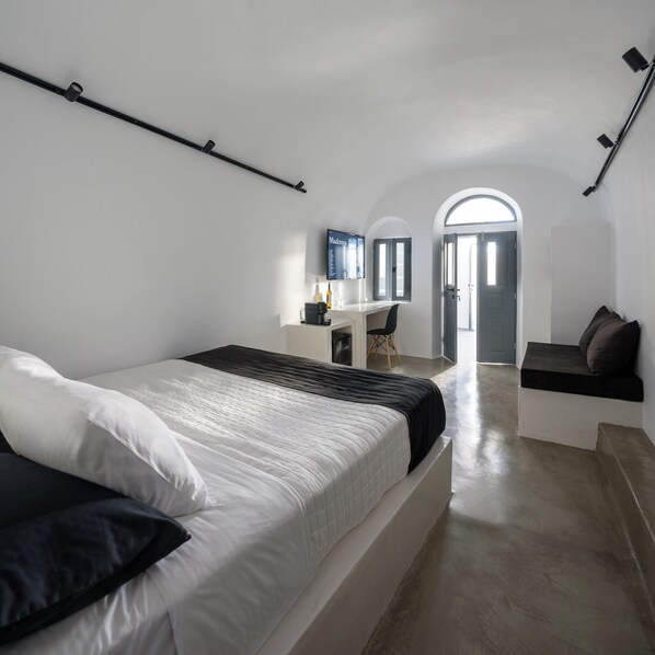 A modern bedroom with a large bed, a desk, and a television.