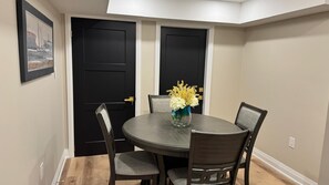 A dining area with a round table, four chairs, and a vase with flowers.