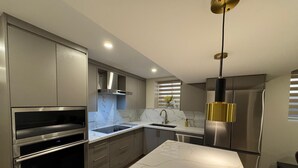 Una cocina moderna con electrodomésticos de acero inoxidable, encimeras de mármol y una lámpara colgante.