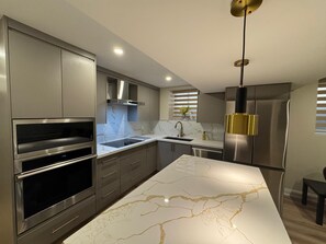 Uma cozinha moderna com eletrodomésticos de aço inoxidável, bancadas de mármore e uma luminária pendente.