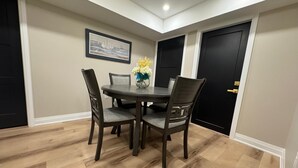 Un comedor con una mesa redonda, cuatro sillas, un jarrón con flores y un cuadro en la pared.