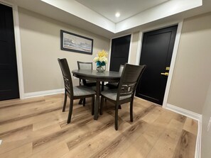Uma sala de jantar com uma mesa redonda, quatro cadeiras, um vaso com flores e um quadro na parede.