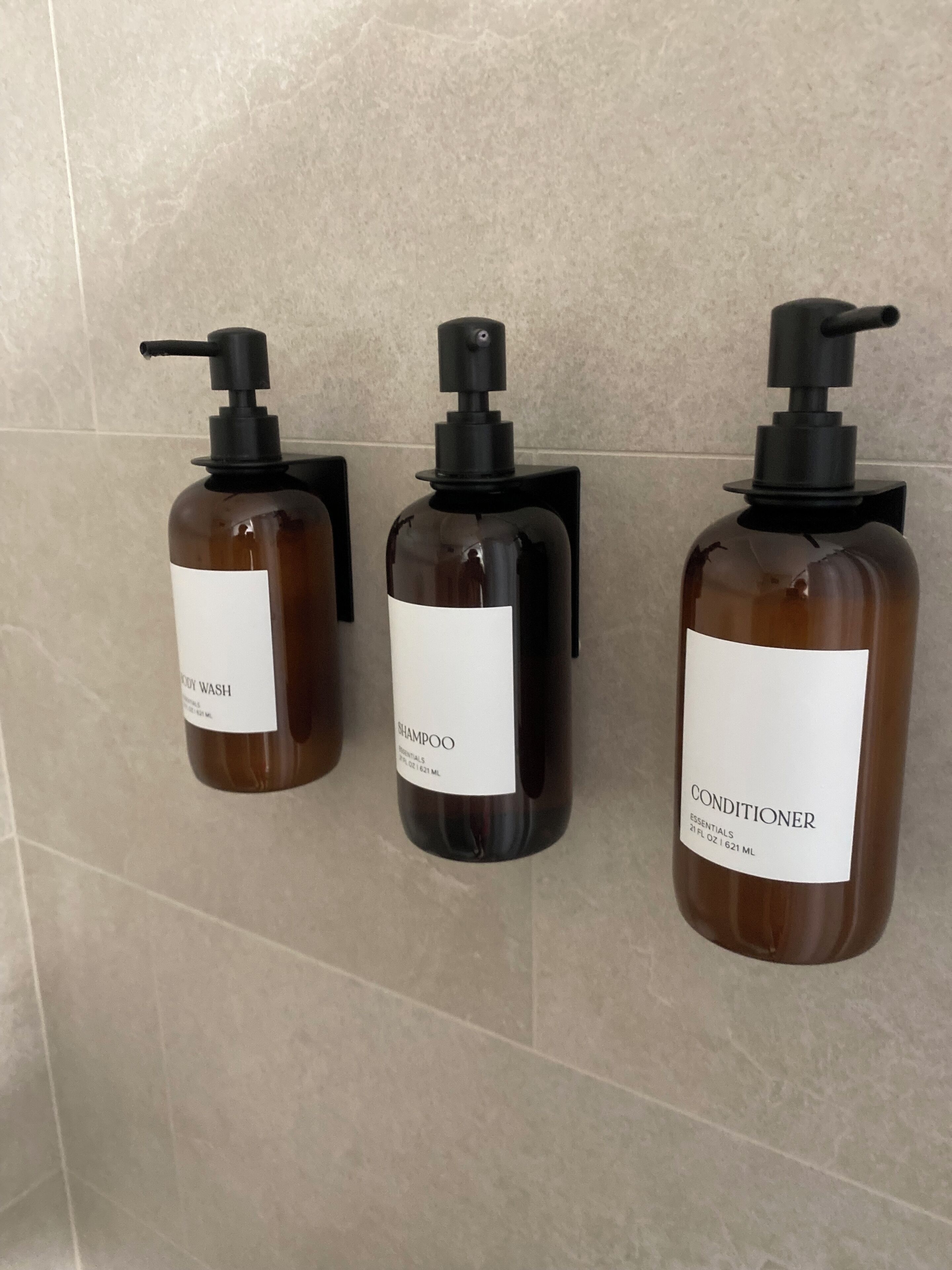 Kolme pulloa hygieniatuotteita on kiinnitetty laatoitettuun seinään.