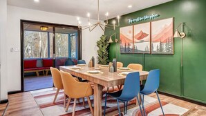 Ein Essbereich mit einem Holztisch, blau-gelben Stühlen, einer grünen Wand mit einem Gemälde und einer roten Bank draußen.