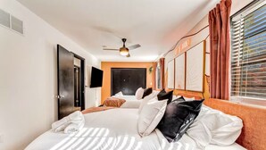 Ein Hotelzimmer mit einem großen Bett, einem Deckenventilator, einem Fernseher und einem Fenster mit Vorhängen.