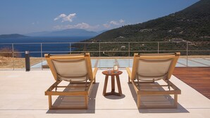 Deux fauteuils de jardin en bois, placés face à une piscine, avec vue sur la mer et les collines.