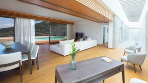 Un salon moderne avec un plafond en bois, un coin repas avec une table et des chaises, un canapé blanc et une vue sur une piscine et des montagnes.