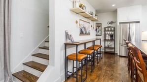 A modern kitchen with a stainless steel refrigerator, wooden bar stools, and a coffee-themed wall art.