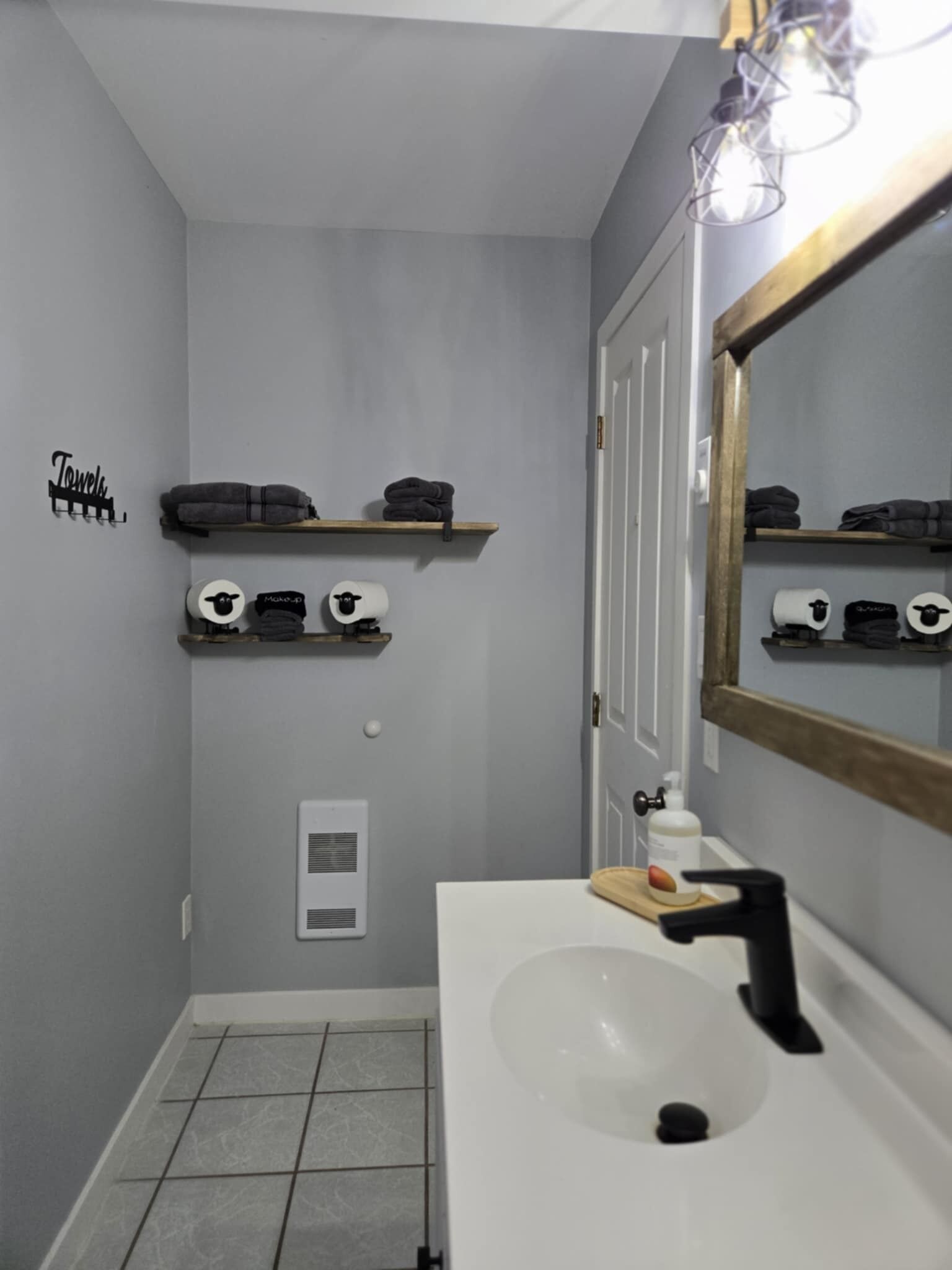 Een badkamer met een witte wastafel, een spiegel en planken met handdoeken en wc-papier.