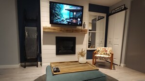 Ett vardagsrum med en TV monterad ovanför en öppen spis, en soffa, ett soffbord och en fåtölj.