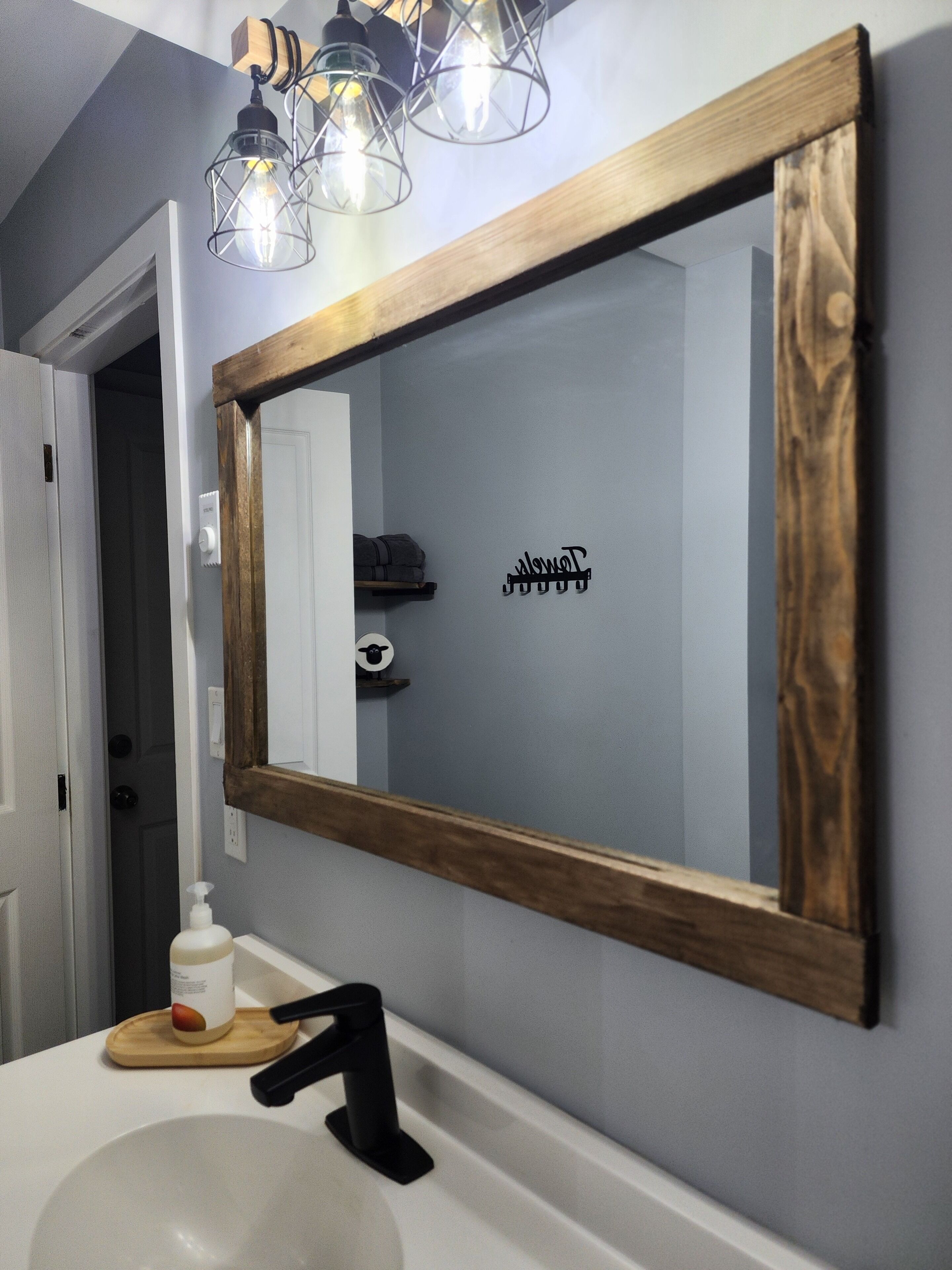Un bagno con uno specchio a cornice in legno, un lavandino bianco e una bottiglia di sapone per le mani.