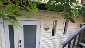 Ett hus med en vit dörr, ett litet fönster med en välkomstskylt och en trätrappa.