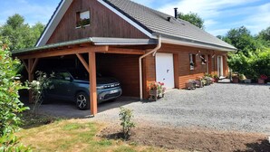 A two-story wooden house with a garage, a gravel driveway, and potted plants.
