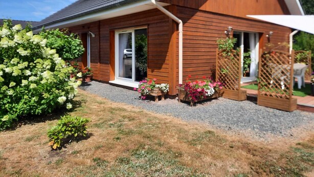 A wooden house with a sloped roof, large windows, and a gravel driveway.