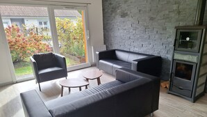 A modern living room with a black leather sofa, two armchairs, a small wooden coffee table, and a stone wall.