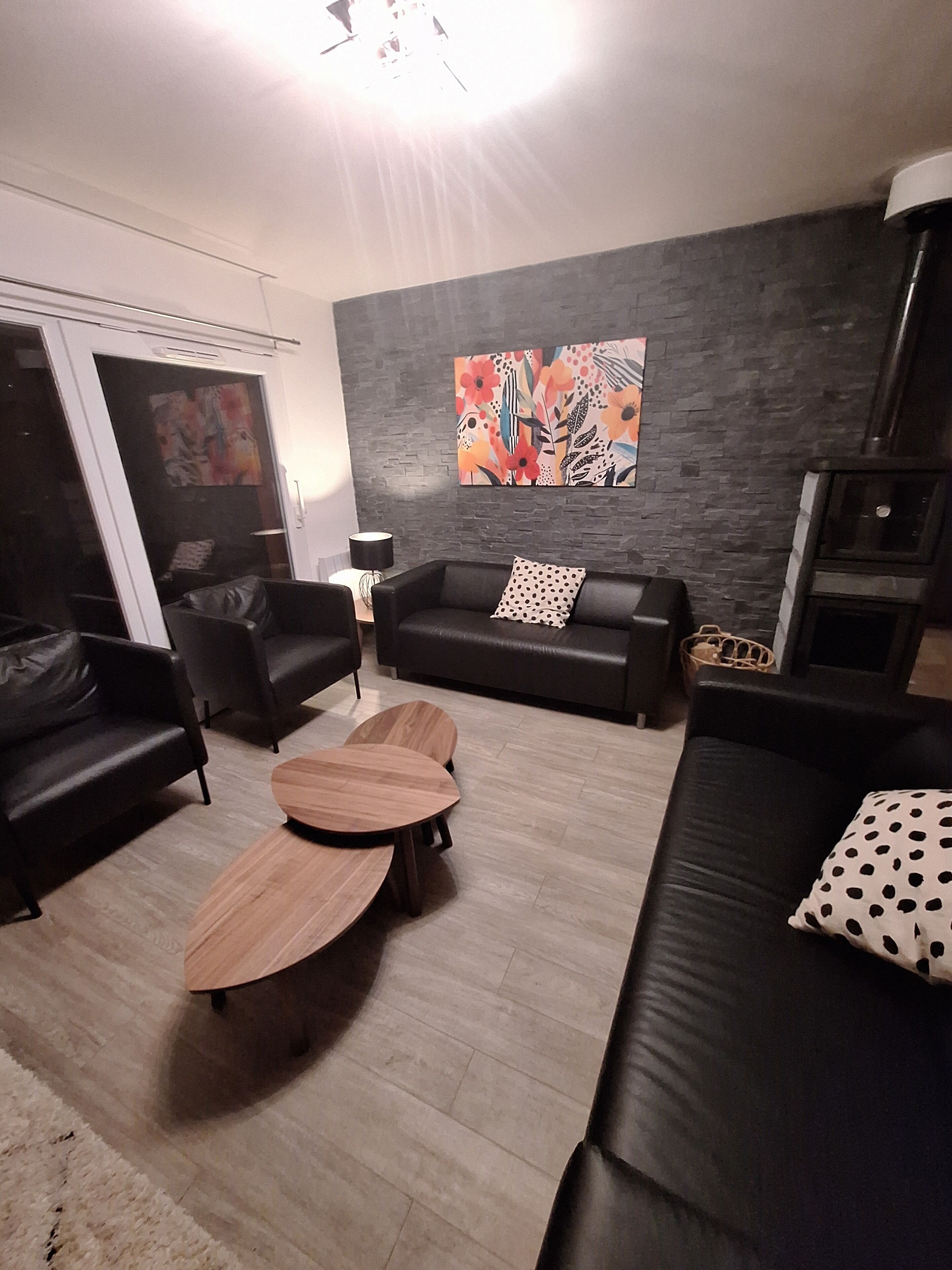 A modern living room with a black leather sofa, a wooden coffee table, and a black leather couch. There is a large abstract painting on the wall and a fireplace.