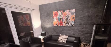 A modern living room with a black leather sofa, a wooden coffee table, and a black leather couch. There is a large abstract painting on the wall and a fireplace.