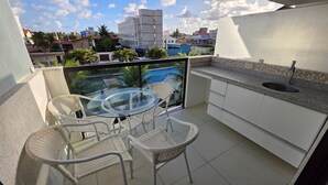 Een balkon met een glazen tafel en rieten stoelen, met uitzicht op een zwembad en gebouwen.