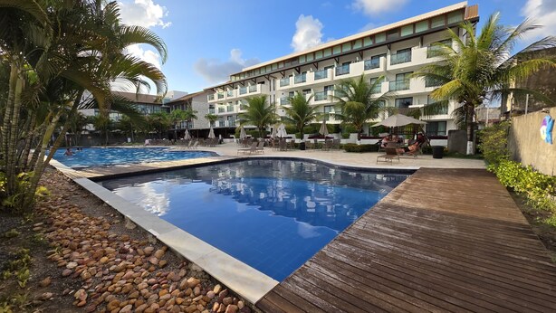 Een hotel met een zwembad, terras en palmbomen.