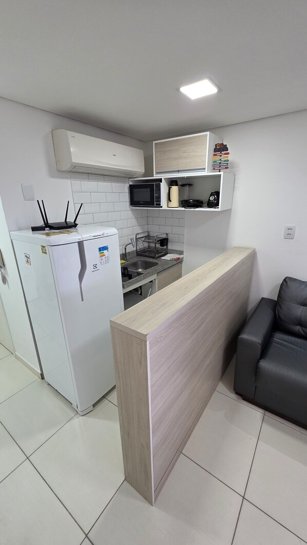 Una cocina moderna con armarios blancos, microondas integrado, refrigerador y encimera de madera.