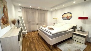 Ein modernes Schlafzimmer mit Holzboden, einem Bett mit weißer Bettwäsche, einem Nachttisch mit Lampe, einer Kommode und einer Wand mit Gemälde und einem Seestern-Dekor.