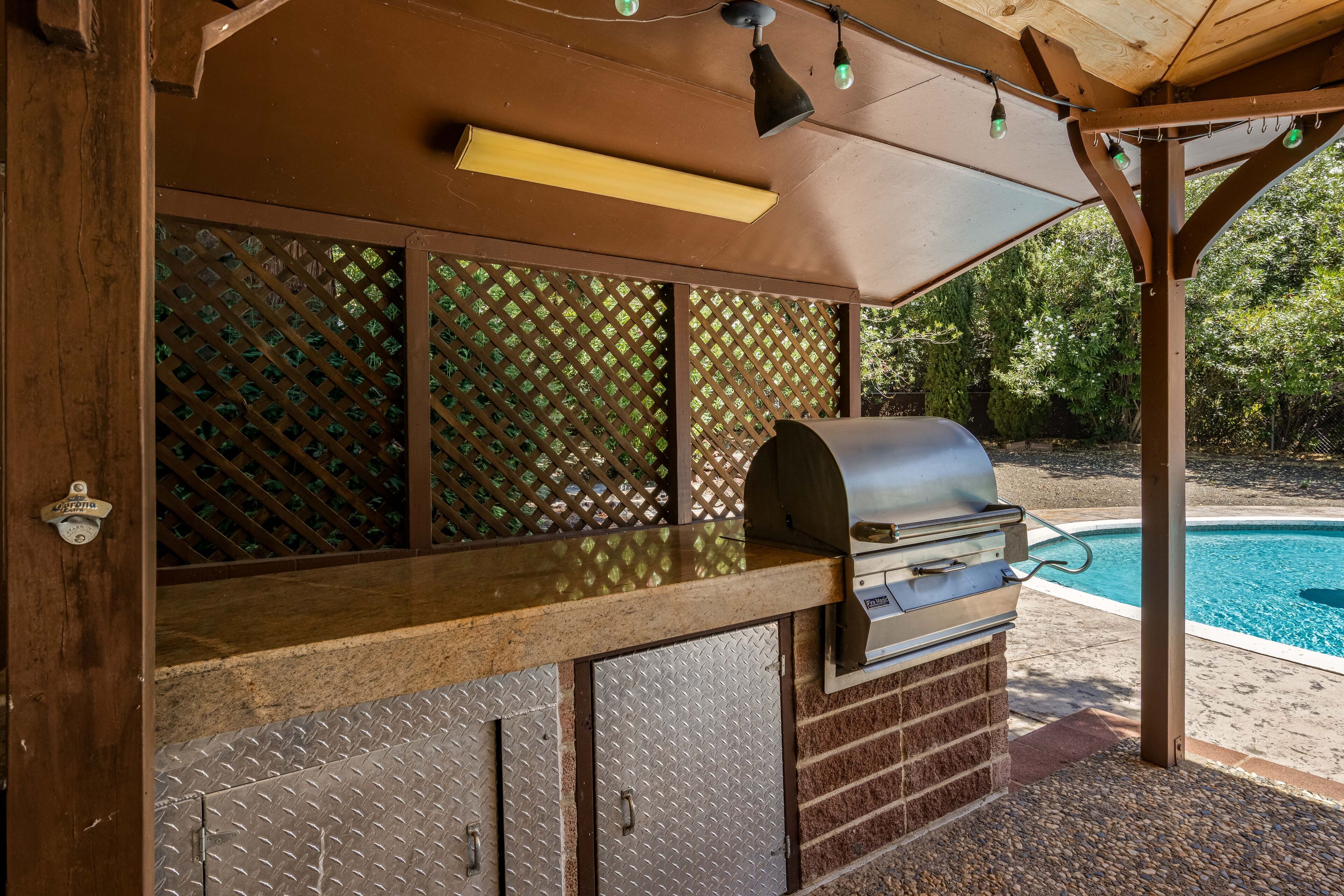 Un espace barbecue extérieur avec un gril, un comptoir en bois et une piscine en arrière-plan.