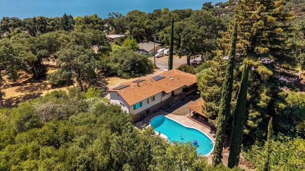 Une maison avec une piscine, entourée d’arbres, qui offre une vue sur un lac et des montagnes.
