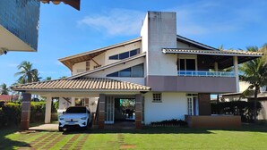 A two-story house with a covered driveway and a car parked in front. - SEASONAL RENTAL BEACH HOUSE ARACAJU SERGIPE CLOSED CONDO FRONT OF THE SEA (Mosqueiro Aracaju)