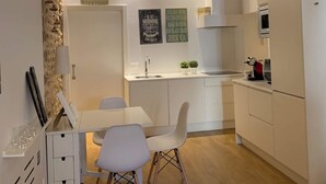Una cocina moderna con armarios blancos, techo de madera y comedor con mesa y sillas blancas.