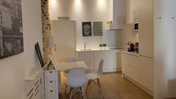 Una cocina moderna con armarios blancos, un comedor con mesa y sillas blancas, y una pared de acento de piedra.